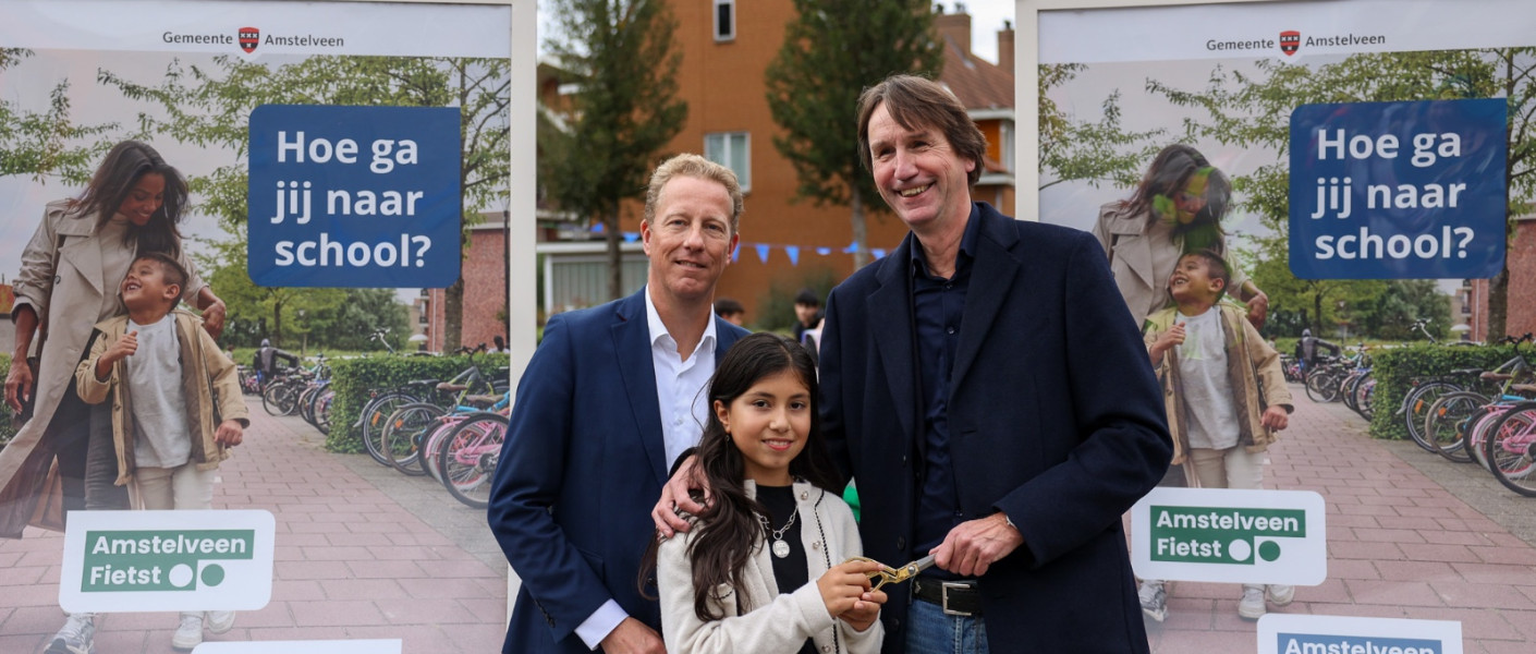 Wethouder Herbert Raat (verkeer) en Frank Berkhout (onderwijs) en kinderburgemeester Velorisa knippen samen het campagnelint door.