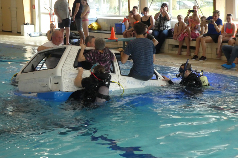De deelnemers klimmen uit de auto die langzaam onder water verdwijnt.