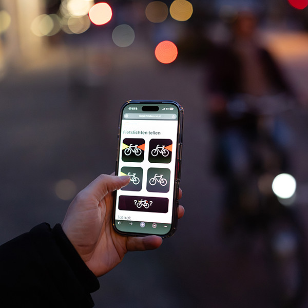 Fietslichtteller op een telefoonscherm in het donker met een fietser met verlichting op de achtergrond