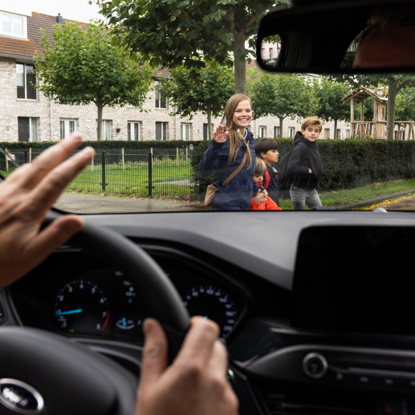 Automobilist zwaait vanuit auto naar overstekende kinderen